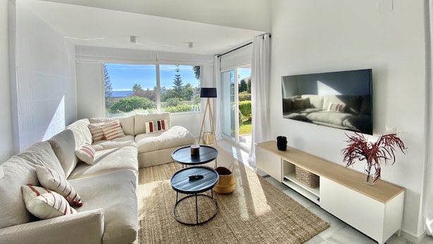Una sala de estar moderna con un sofá grande, una mesa de centro, un televisor y vistas al exterior.
