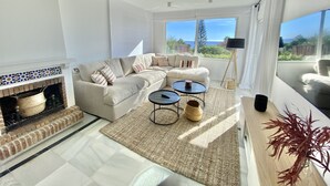 Un salón espacioso con un sofá grande, una mesa de centro y una chimenea. Se aprecia una ventana grande con vistas al exterior.