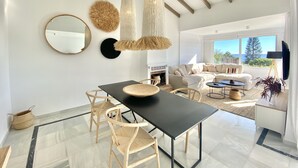 Una sala de estar moderna con una mesa de comedor negra, sillas de madera, chimenea, sofá y televisor.