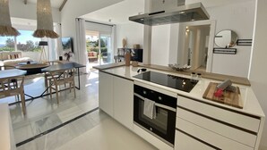 Una cocina moderna con una isla central, horno empotrado y un amplio ventanal con vistas a un jardín.