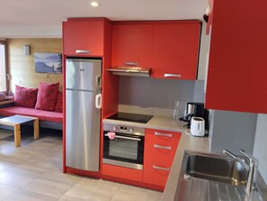 Une cuisine compacte avec des meubles de rangement rouges, un réfrigérateur en acier inoxydable, un four encastré et un évier.