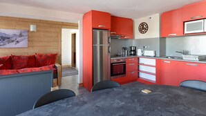 A modern kitchen with red cabinets, a stainless steel refrigerator, a microwave, and a coffee maker. There is a dining table with chairs and a wooden floor. - Bright Apartment · Near Slopes · Balcony · Pets Allowed (La Plagne Montchavin Les Coches)