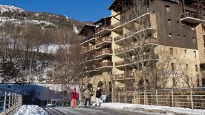 Ein mehrstöckiges Gebäude mit Balkonen, ein Sessellift im Hintergrund und eine verschneite Landschaft.