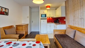 A compact living space with a kitchenette, a sofa, a dining table, and a wooden accent wall. - Bright apartment with balcony in the station center (Flaine)