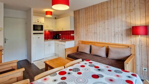 A compact hotel room with a kitchenette, a wooden headboard bed, a small table, and a red lamp. - Bright apartment with balcony in the station center (Flaine)