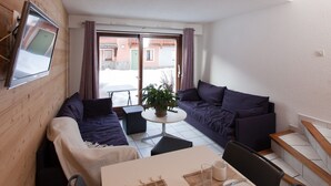 A modern living room with a sofa set, a dining table, and a TV mounted on the wall.
