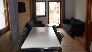 A compact room with a white table and chairs, a sofa, and a TV mounted on the wall.