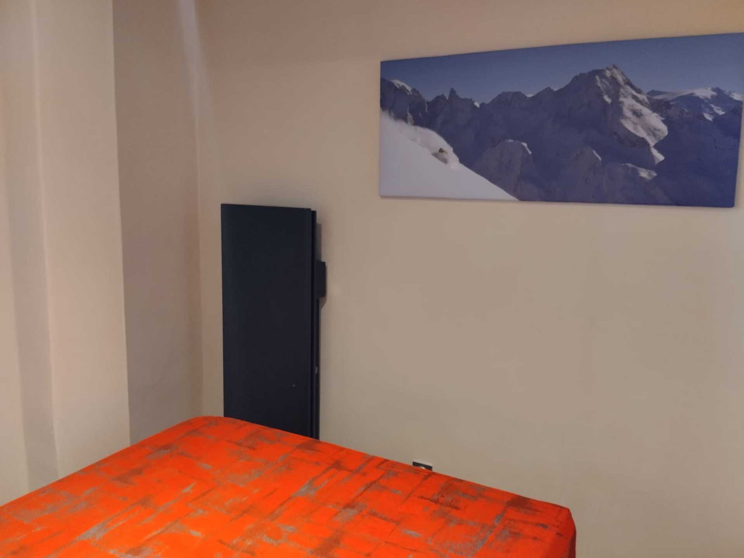 A room with a bed, a black cabinet, and a mountain landscape painting on the wall.