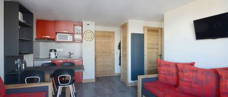 Un espacio habitable compacto con kitchenette, comedor y sala de estar con un sofá rojo.