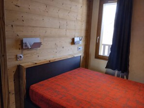 A room with a bed, a wooden headboard, a window with curtains, and a wall-mounted electrical outlet. - Renovated apartment 5 pers, pets allowed, near slopes (La Plagne Montchavin Les Coches)