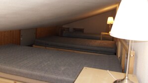 Une petite pièce mansardée, faiblement éclairée, avec deux lits superposés et une petite table de chevet.