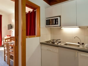 Cozinha compacta com micro-ondas, fogão, pia e cadeiras de madeira.