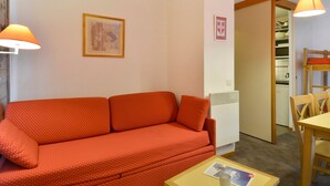 Un salon avec un canapé rouge, un tableau encadré au mur et un coin repas comprenant une table et des chaises.