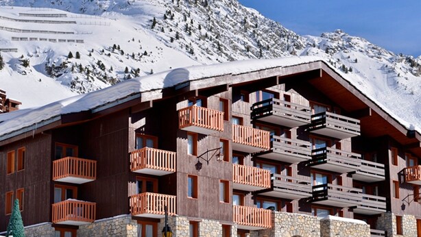 Un immeuble en bois à plusieurs étages, doté de balcons, se dressant sur fond de montagnes enneigées.