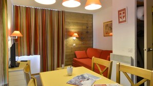 Une pièce avec une table jaune, des lampes orange, des rideaux à rayures, un mur en bois et un canapé rouge.