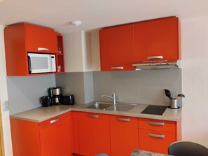 A compact kitchen with red cabinets, a microwave, a coffee maker, and a sink. - Renovated apartment near slopes, balcony, pets ok (La Plagne Montchavin Les Coches)