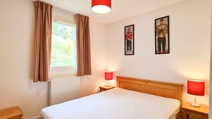 Une chambre à coucher avec un lit en bois, deux tables de chevet avec des lampes, une fenêtre avec des rideaux et deux tableaux encadrés accrochés au mur.