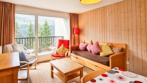 Une pièce chaleureuse avec un mur en bois, une lampe rouge, un canapé avec des coussins, une table en bois et une chaise.
