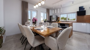 A modern dining area with a glass table, six chairs, and a chandelier. - Villa Dora (Policnik)