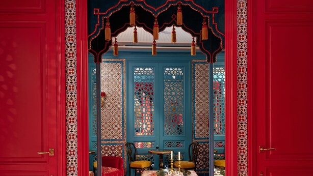 Um quarto com piso xadrez, porta vermelha e divisória azul com desenhos elaborados.
