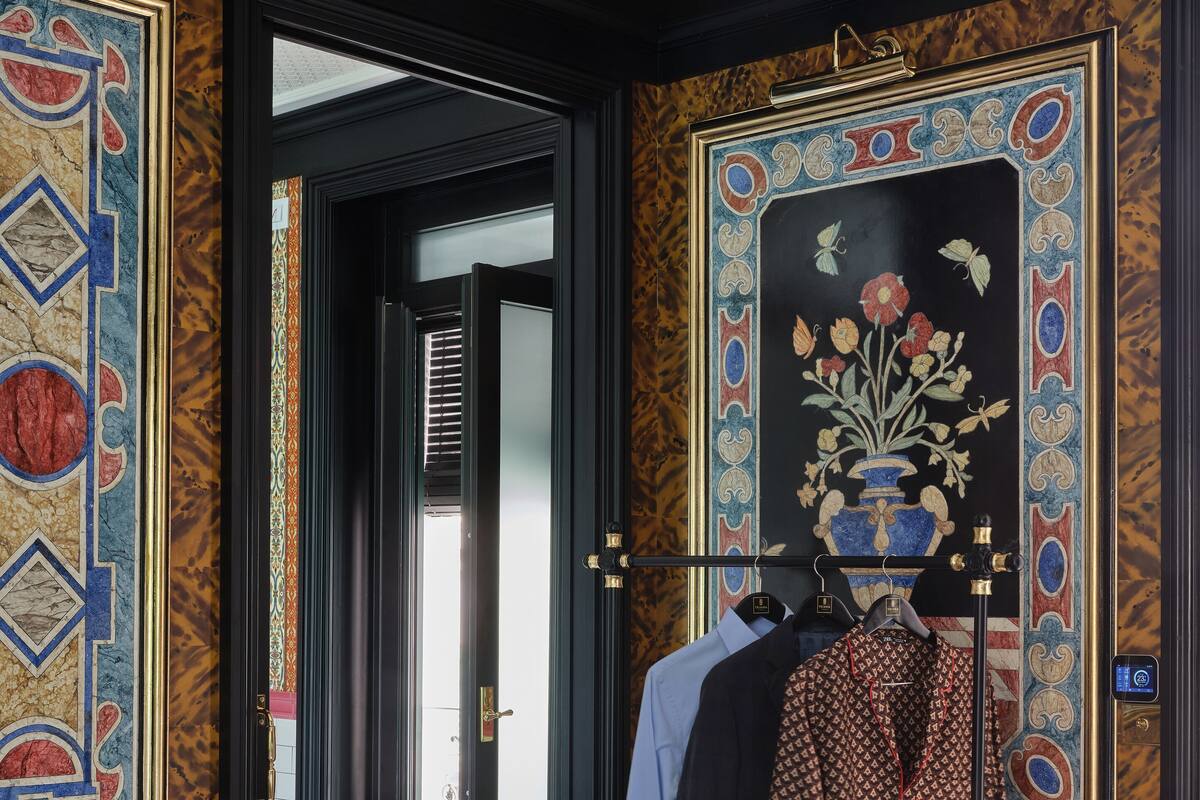Une pièce avec un mur orné de motifs, un mannequin portant des vêtements et une porte donnant sur une autre pièce.