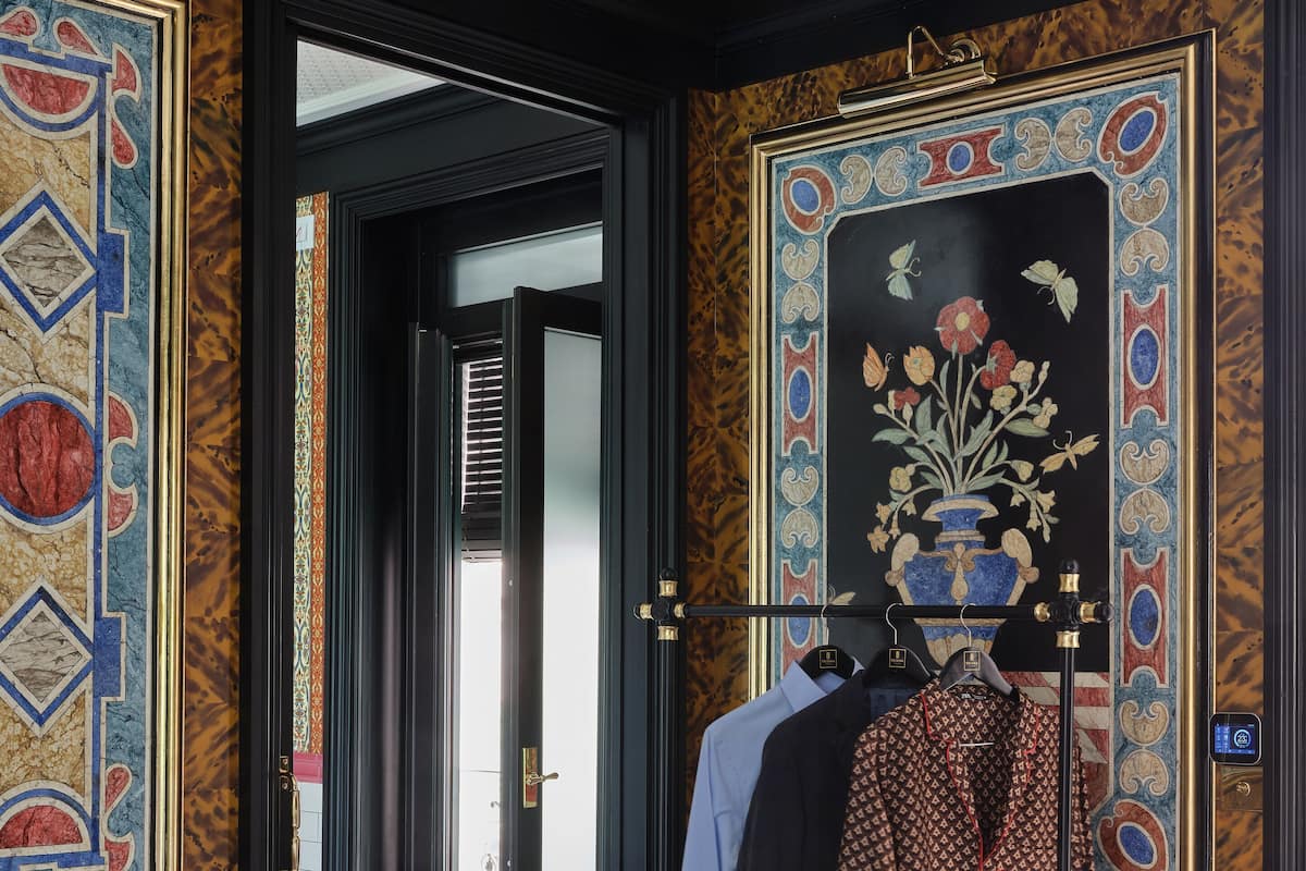 Una stanza con una parete decorata, un manichino vestito e una porta che dà su un'altra stanza.
