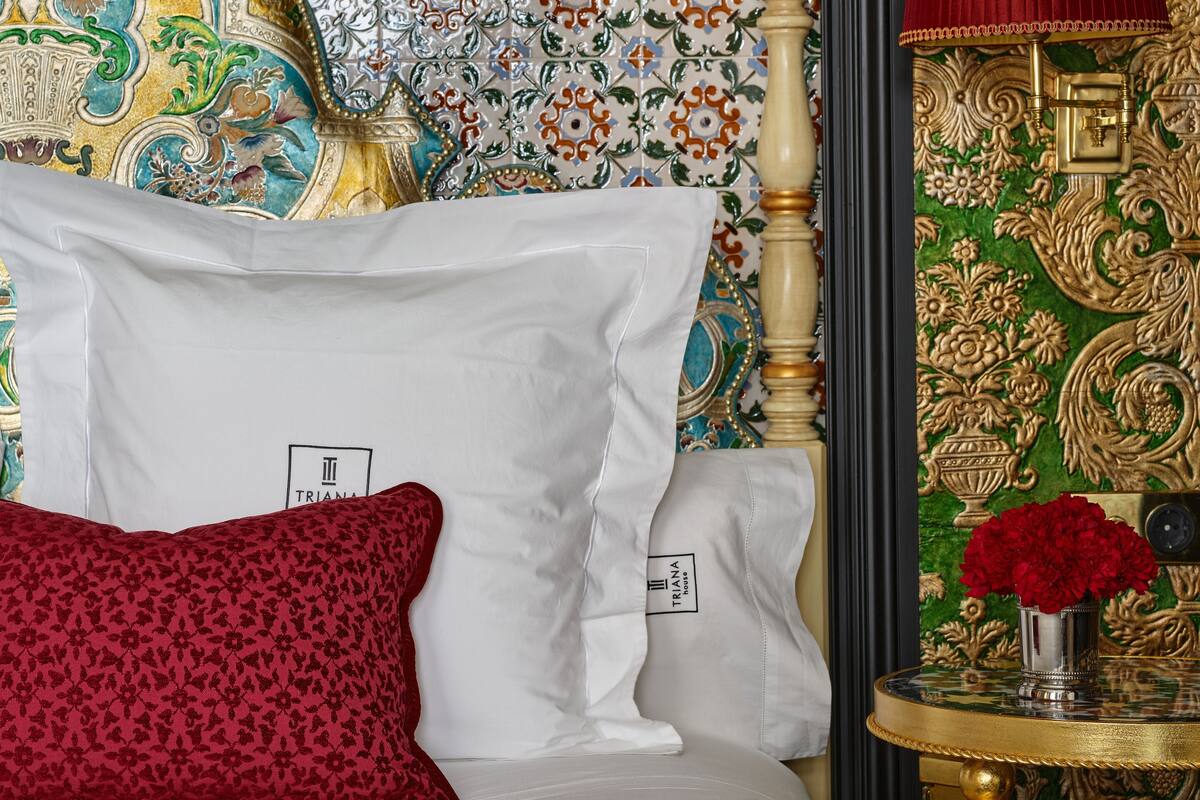 Un lit avec des oreillers blancs et rouges, un oreiller à motifs floraux rouges et une tête de lit avec un cadre doré.