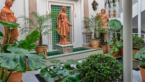 Pátio com estátua central, rodeado por plantas em vasos e piso de azulejos.