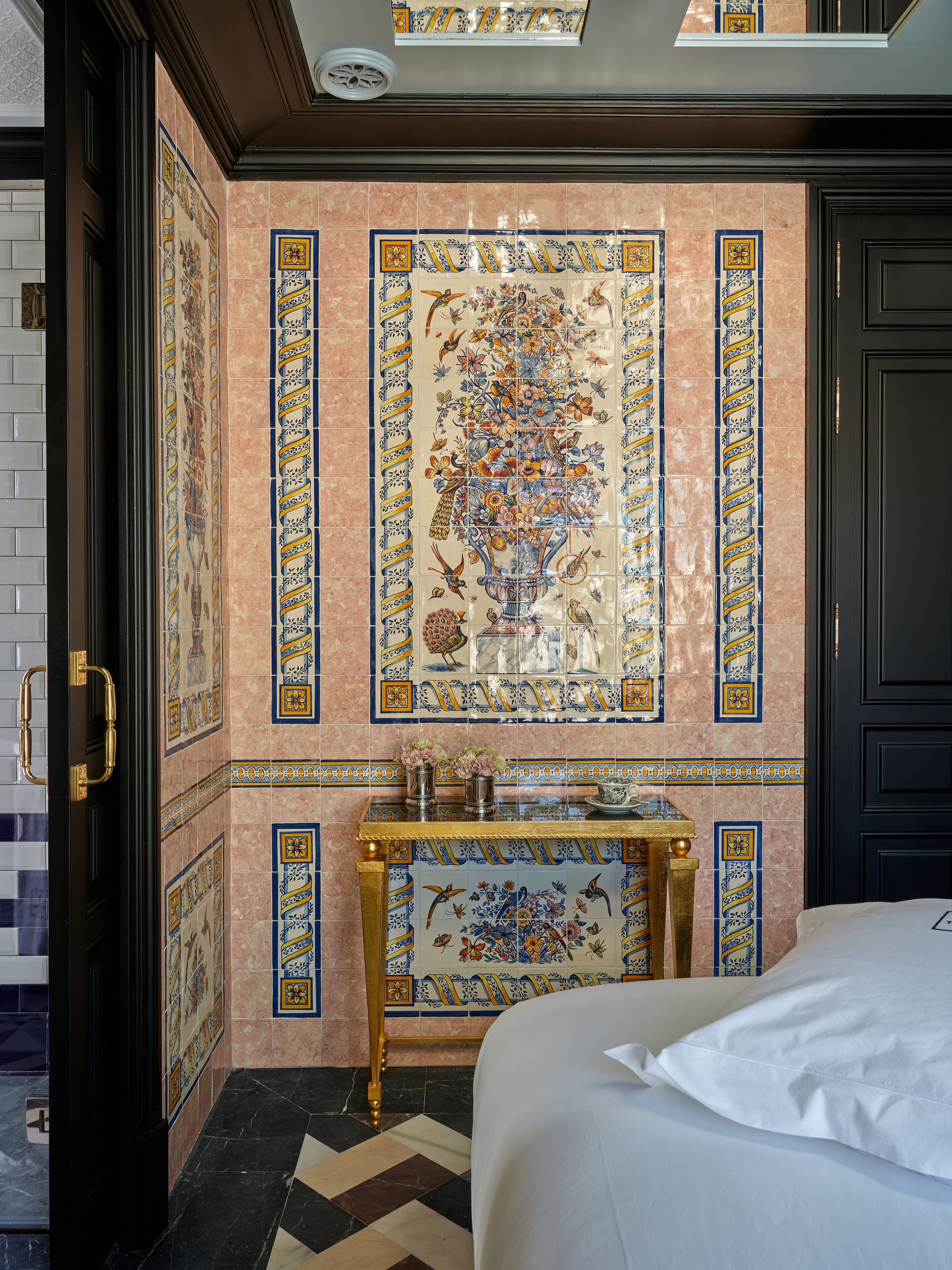 A hotel room with a bed, a small table with a vase, and a decorative tile wall.