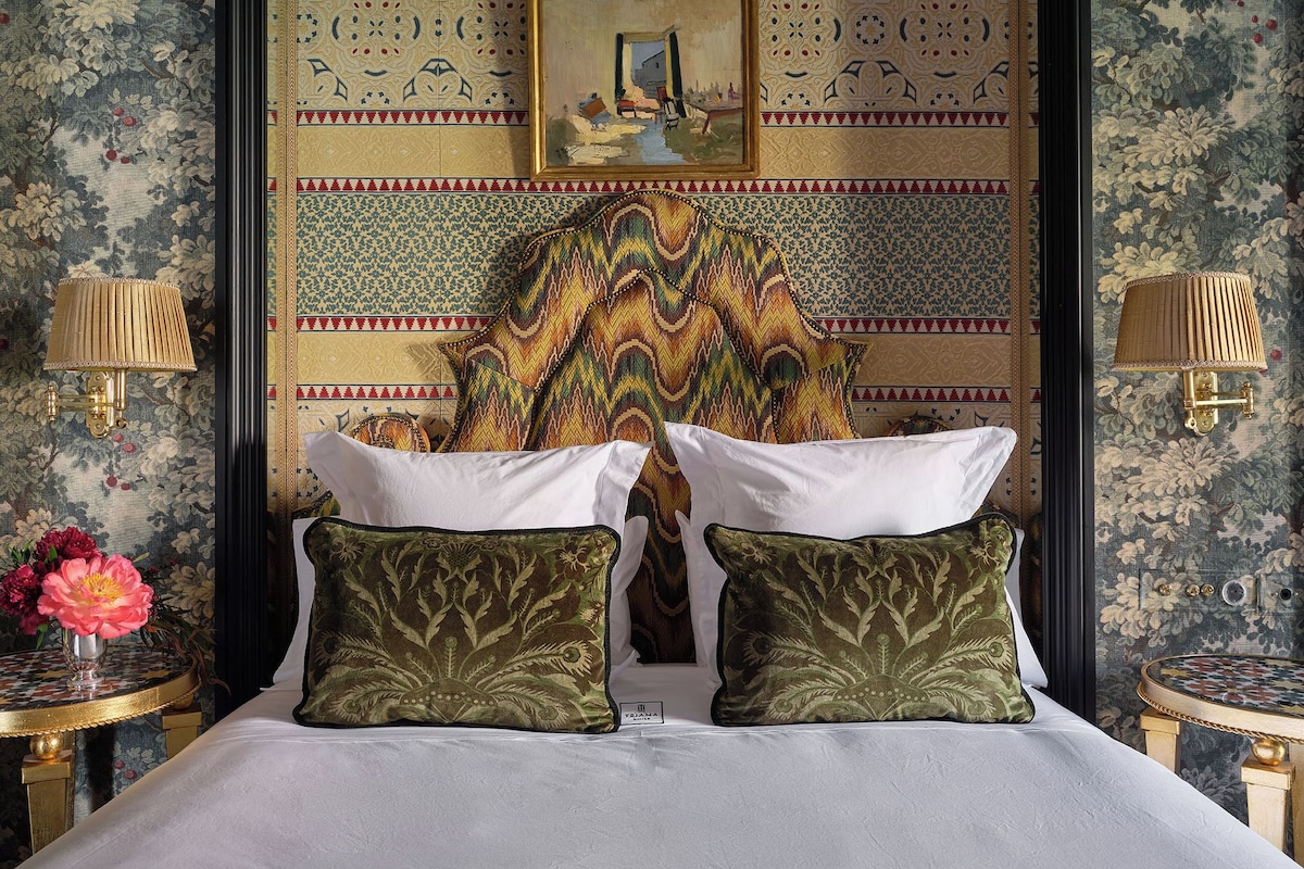 Habitación de hotel con una cama, dos almohadas, un cuadro en la pared y dos lámparas de pared.