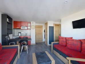 A compact living space with a kitchenette, a dining area, and a sofa with red cushions. - Renovated apartment near slopes with free parking (La Plagne Montchavin Les Coches)
