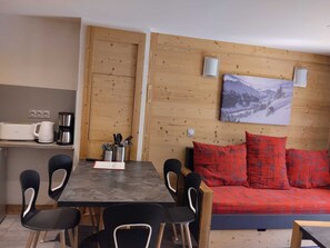 A modern living space with a dining area, a sofa with red cushions, and a wall-mounted picture. - Renovated apartment near slopes with free parking (La Plagne Montchavin Les Coches)