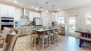 Una cocina moderna con armarios blancos, una isla central con taburetes, electrodomésticos de acero inoxidable y un salpicadero de azulejos tipo espiga.