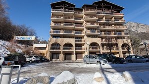 A multi-story hotel with balconies, a parking lot, and a mountainous backdrop.