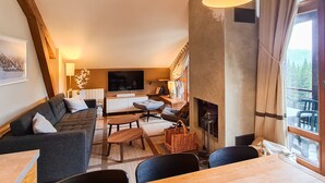Ein gemütliches Wohnzimmer mit Sofa, Fernseher, Kamin und Essbereich.