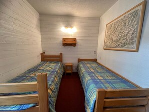 Una habitación pequeña y acogedora con dos literas de madera, una mesita de noche de madera y un estante fijado a la pared.