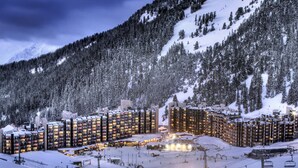 Estació d'esquí amb paisatge nevós, diversos blocs d'edificis alts, telefèrics i un paisatge de muntanyes.