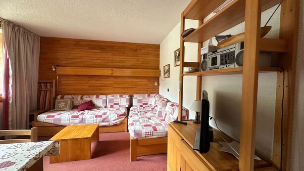 Habitació acollidora amb dos llits, un escriptori de fusta, una estant amb un aparell de ràdio i una finestra amb cortines.
