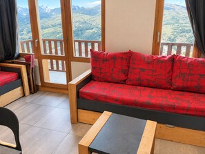 Ein Zimmer mit einer Couch, einem kleinen Tisch und Blick auf eine gebirgige Landschaft durch große Fenster.