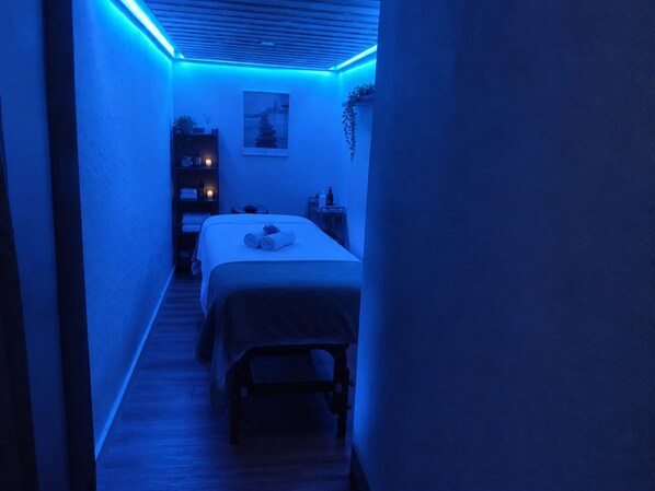 Un pasillo estrecho que conduce a una cama con cabecera, una mesita de noche y un estante en la pared con objetos.