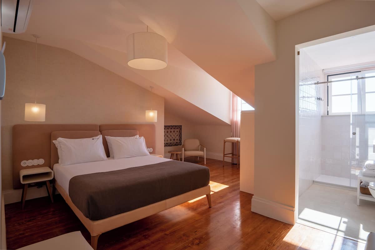 Un dormitorio moderno con una cama grande, mesitas de noche, una silla y vistas al baño.