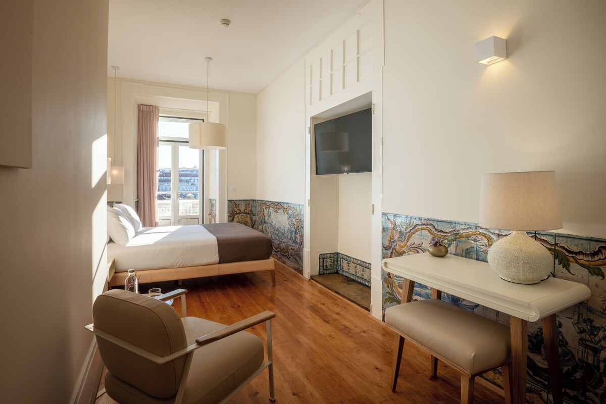 Une chambre d’hôtel avec un lit, un bureau, une chaise, une télévision et une fenêtre avec des rideaux.
