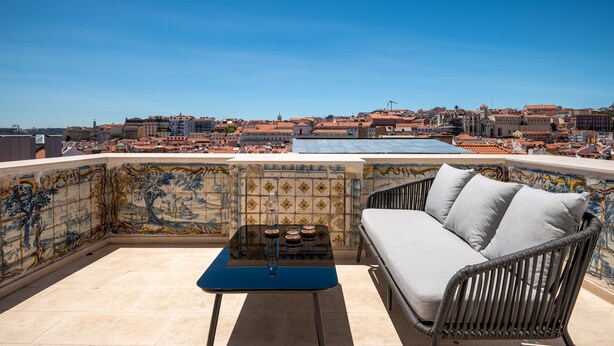Una terraza en la azotea con un sofá de mimbre, una mesita pequeña y un muro de azulejos con diseño de mosaico.