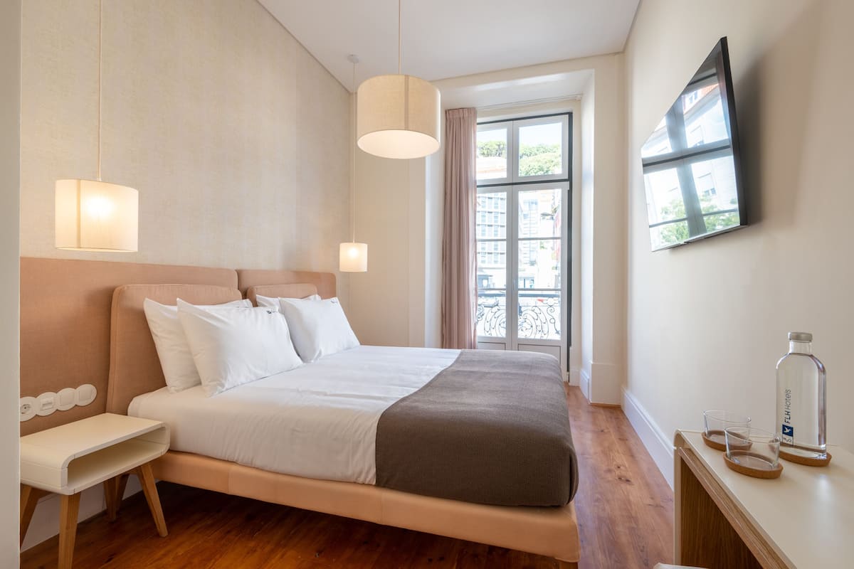 Una habitación de hotel moderna con una cama grande, mesitas de noche, un televisor y una ventana con vistas.
