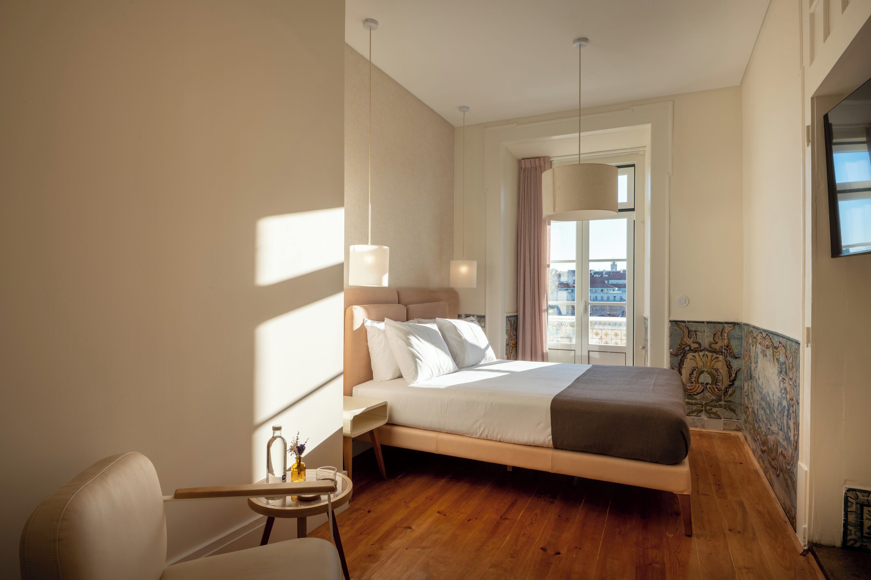 A modern hotel room with a large bed, a small round table, and a view of the city through the window.