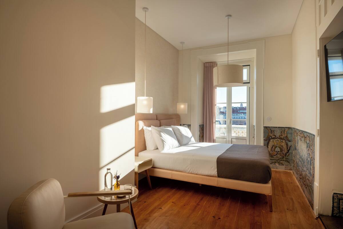 Una habitación de hotel moderna con una cama grande, una pequeña mesa redonda y vistas a la ciudad a través del ventanal.