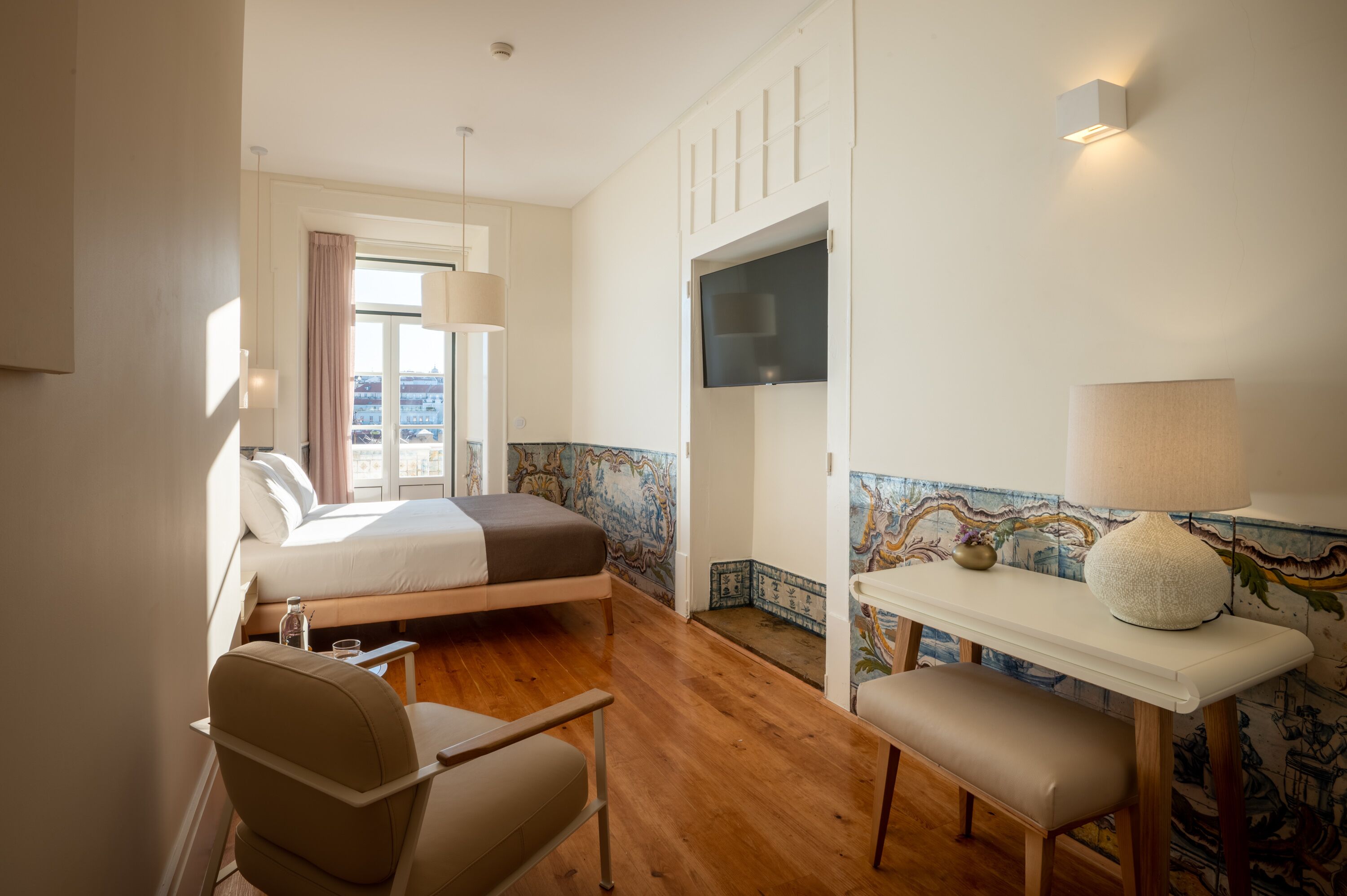 A hotel room with a bed, a desk, a chair, a TV, and a window with curtains.