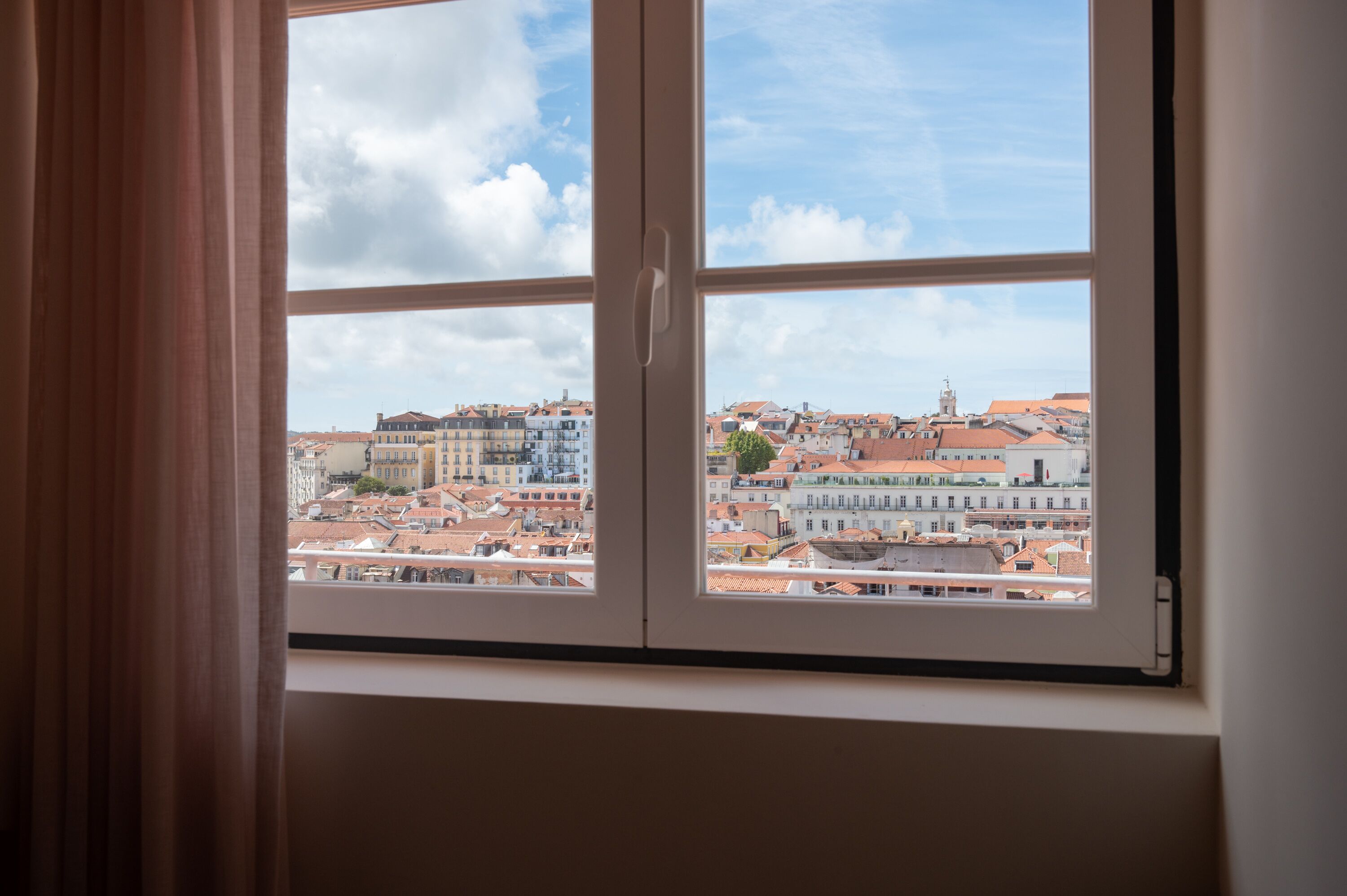 A window with a view of a cityscape, featuring multiple buildings and a clear sky.