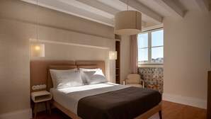 Un dormitorio ordenado con una cama grande, mesitas de noche, una silla y una ventana con vistas.