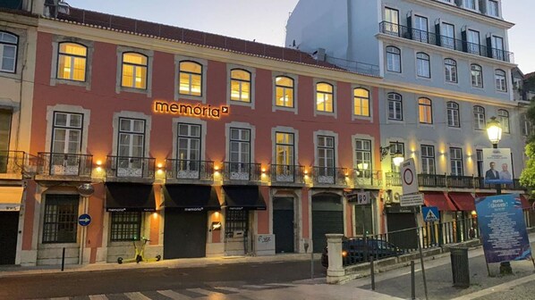 Un immeuble avec une enseigne au néon indiquant le mot « memória » au rez-de-chaussée, doté de nombreuses fenêtres et de balcons.